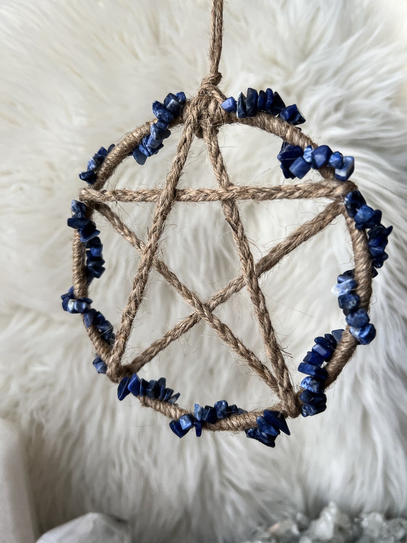 May include: A handmade dreamcatcher with a brown jute rope base and a five-pointed star design. The dreamcatcher is decorated with a circle of blue lapis lazuli stones.