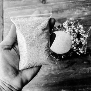 May include: A clear plastic bag filled with small, white, round beads. The bag is held in a hand.