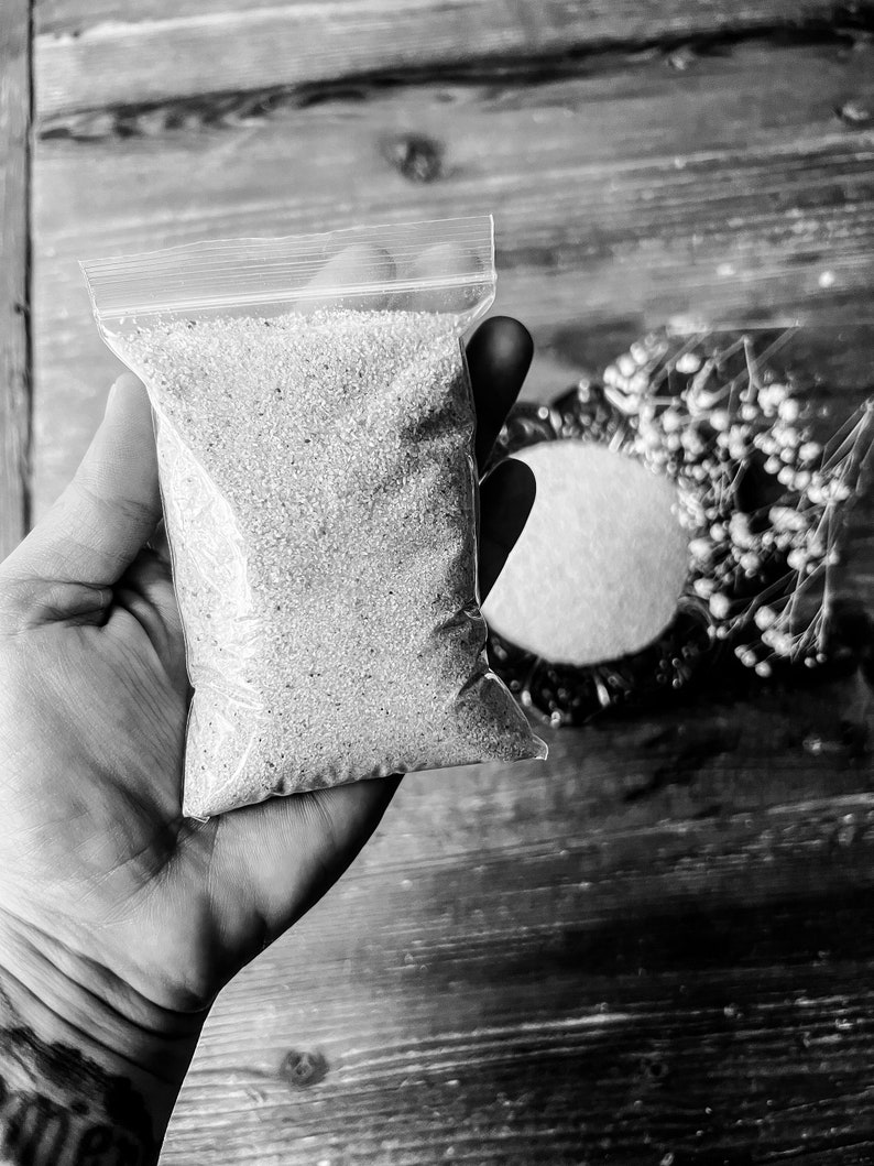 May include: A clear plastic bag filled with small, white, round beads. The bag is held in a hand.