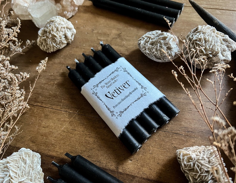 May include: A package of five black vetiver candles. The candles are wrapped in white paper with black text that reads 'The Stone Middens Candles Vetiver Protection, Abundance & Grounding'.
