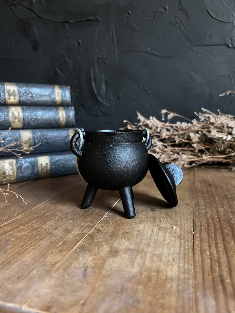 May include: A small black cauldron with three legs and a lid. The cauldron is made of cast iron and has a rustic look.