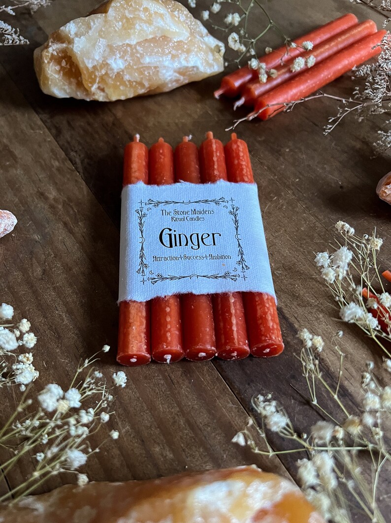 K&ouml;nnte beinhalten: Sechs rote Ingwer-Ritualkerzen, die mit einem wei&szlig;en Etikett zusammengebunden sind, auf dem "The Stone Maidens Ritual Candles Ginger Attraction + Success + Ambition" steht.