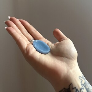 May include: A light blue oval-shaped crystal palm stone. The stone is smooth and polished.