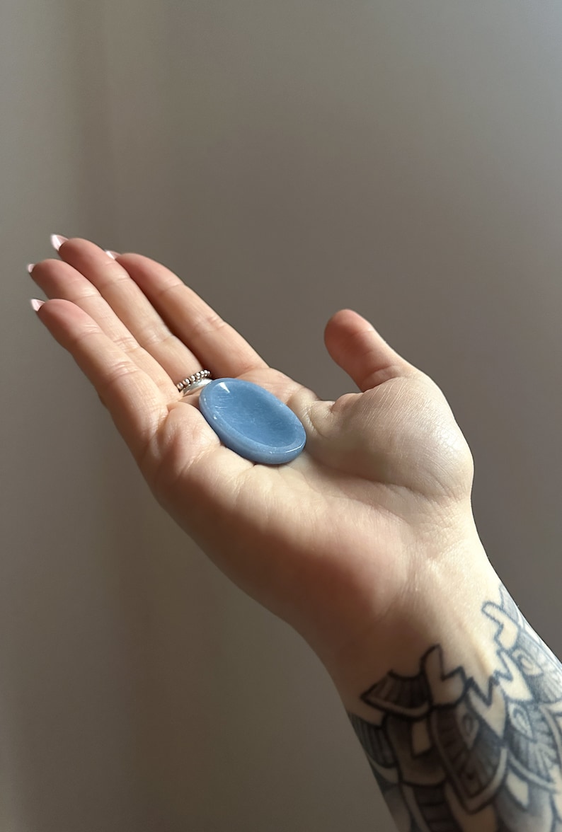 May include: A light blue oval-shaped crystal palm stone. The stone is smooth and polished.