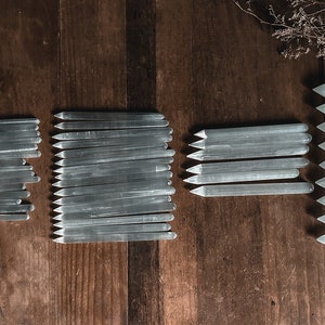 May include: A collection of selenite wands, also known as selenite sticks, arranged on a wooden surface. The wands are various lengths and are all white and translucent.
