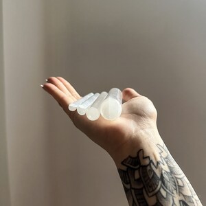 May include: Five white selenite wands of varying lengths, stacked on top of each other, held in a hand.