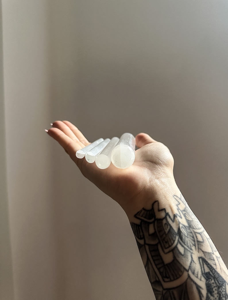 May include: Five white selenite wands of varying lengths, stacked on top of each other, held in a hand.