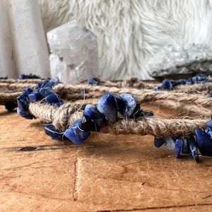 May include: A blue and white crystal heart-shaped wall hanging made with natural twine and blue sodalite stones.