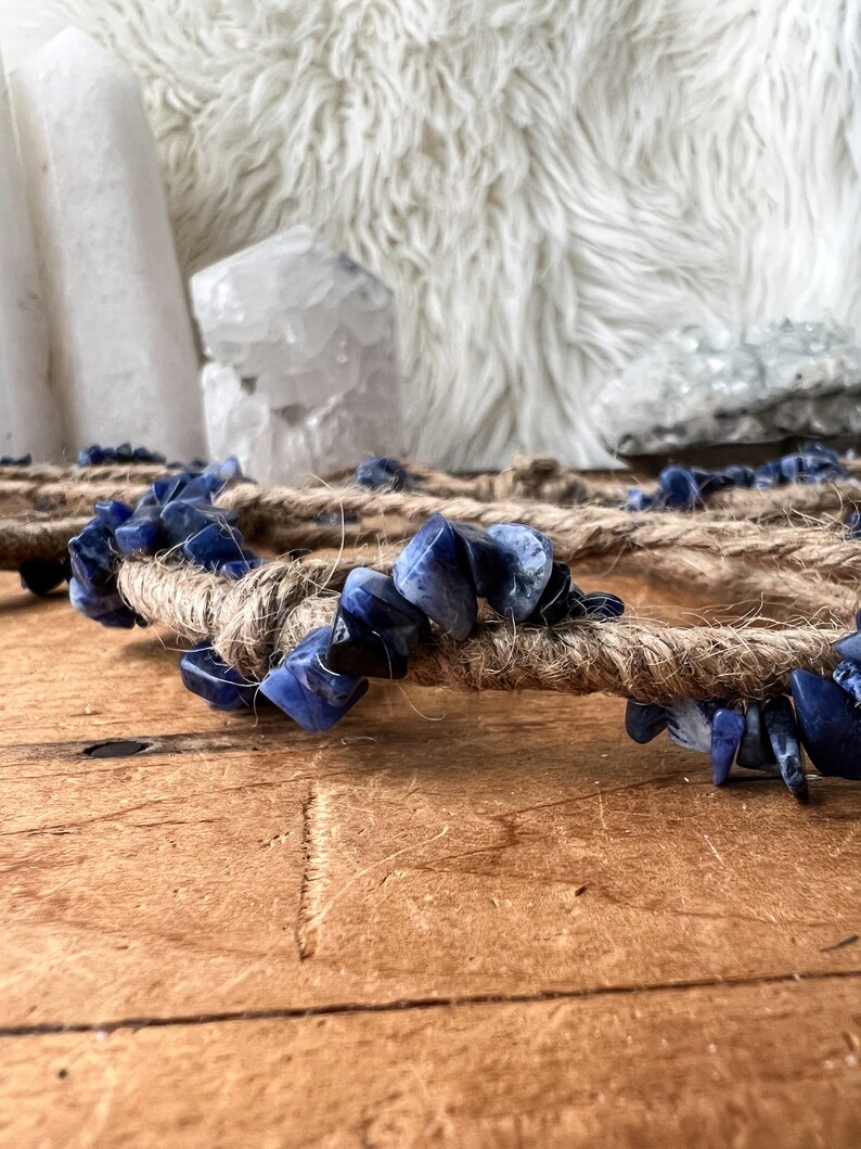 May include: A blue and white crystal heart-shaped wall hanging made with natural twine and blue sodalite stones.