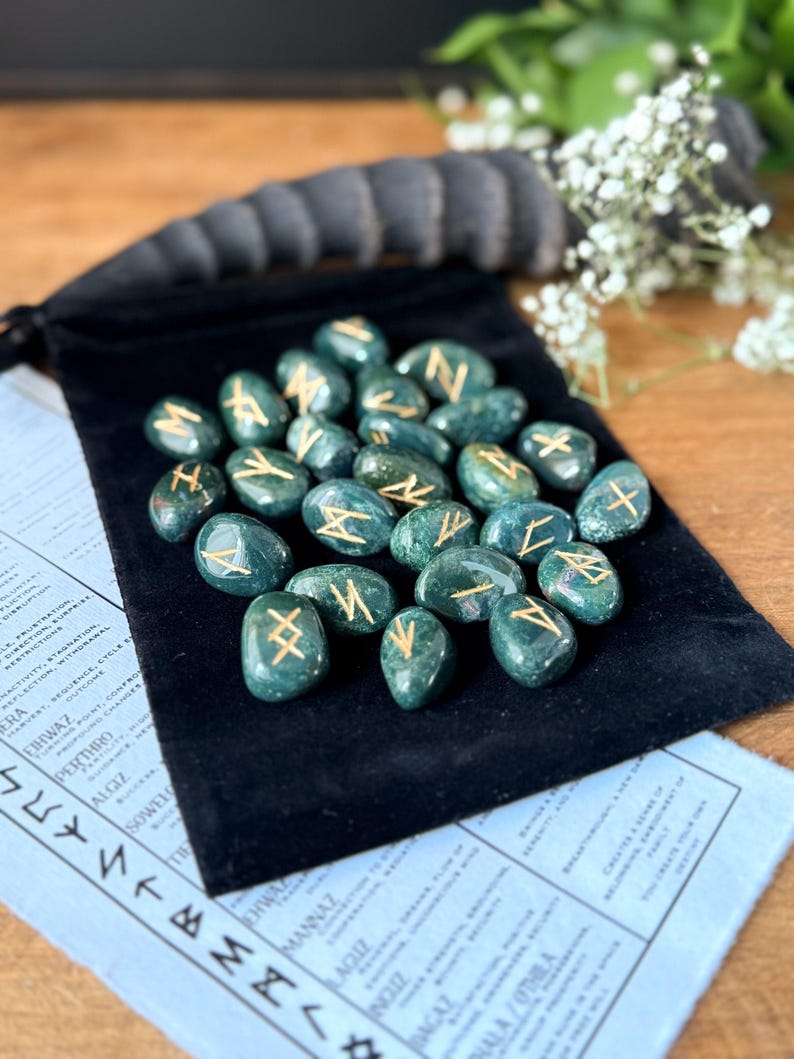 May include: A set of 25 green agate rune stones with gold lettering on each stone. The stones are in a black velvet pouch.