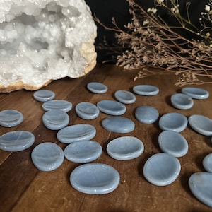 May include: A collection of smooth, light blue, oval-shaped polished stones. The stones are arranged on a wooden surface.