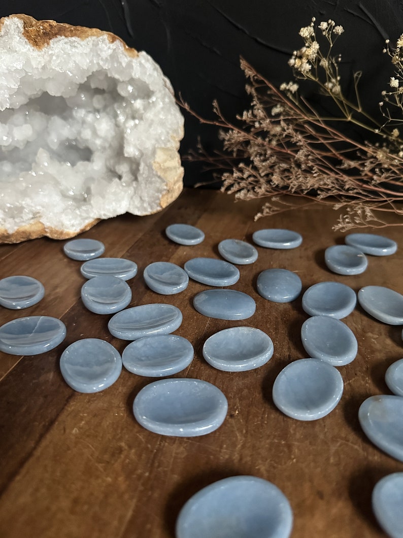 May include: A collection of smooth, light blue, oval-shaped polished stones. The stones are arranged on a wooden surface.