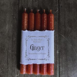 K&ouml;nnte beinhalten: Ein Set mit sechs orangefarbenen Ingwer-Ritualkerzen, verpackt in wei&szlig;em Stoff mit einem Etikett mit der Aufschrift "The Stone Maidens Ritual Candles Ginger Attraction + Success + Ambition".