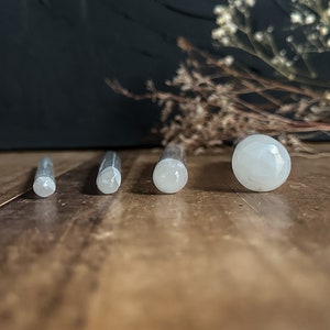May include: Four white, smooth, cylindrical plugs of varying sizes, made of polished stone, on a wooden surface. The largest plug has a rounded top.