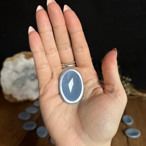 May include: A light blue oval-shaped stone with a silver rim and a white diamond shape in the center.