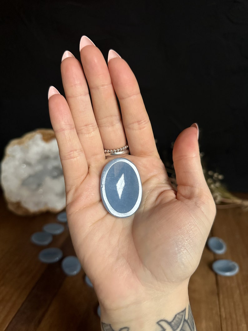 May include: A light blue oval-shaped stone with a silver rim and a white diamond shape in the center.