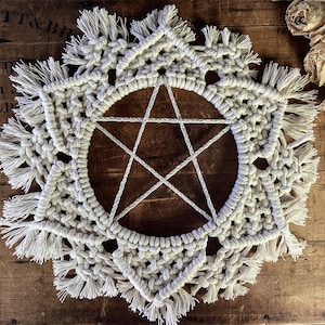 May include: A white macrame wall hanging with a five-pointed star design and fringe details.