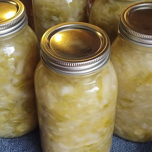 May include: Five glass jars filled with fermented cabbage, also known as sauerkraut. The jars have silver lids and are arranged on a blue surface.