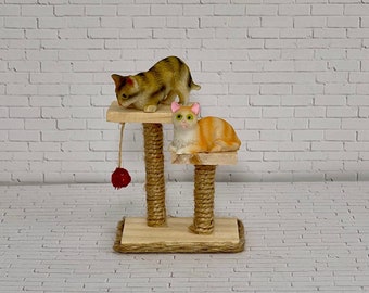 Pode incluir: Uma árvore para gatos em miniatura com duas plataformas e um brinquedo vermelho pendurado. Um gato tigrado marrom está na plataforma superior e um gato branco e laranja está na plataforma inferior.