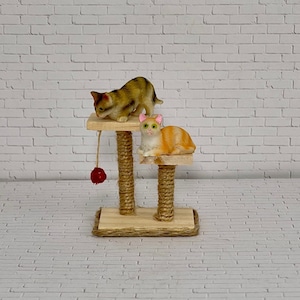 May include: A miniature cat tree with two platforms and a dangling red toy. A brown tabby cat is on the top platform and a white and orange cat is on the lower platform.