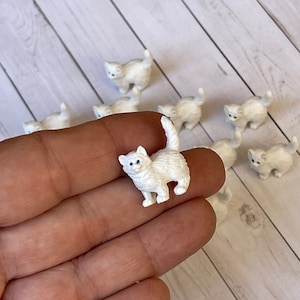 May include: A set of ten miniature white ceramic kittens with blue eyes. The kittens are in various poses and are approximately 1 inch tall.