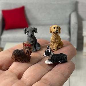 May include: Four miniature dog figurines, including a grey Weimaraner, a brown Yorkshire Terrier, a black and white Boston Terrier, and a light brown Golden Retriever. The figurines are sitting on a hand.