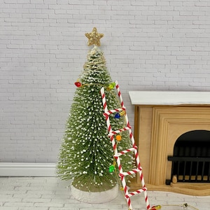 May include: Miniature Christmas tree with a gold star topper, decorated with colorful lights. A candy cane striped ladder leans against the tree. A string of miniature lights is on the floor, near a miniature fireplace.