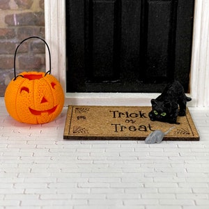 May include: An orange jack-o'-lantern with a black handle sits on a white brick surface next to a brown doormat with the text "Trick or Treat" on it. A black cat with green eyes and a gray mouse are on the doormat.
