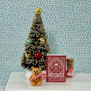 May include: Miniature Christmas scene with a decorated tree, ornaments, and a small teddy bear holding a candy cane. A red box with the text "PEPPERMINT A CANDY CANE ADVENTURE" and a jar of candy are also present.