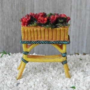 May include: A miniature yellow planter with red flowers sits on a yellow stand with blue accents. The planter and stand are made of resin and are perfect for a miniature garden or fairy garden.