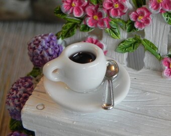 May include: A miniature white teacup and saucer with a silver spoon, filled with dark liquid, sits on a white bench. The bench is decorated with pink flowers and green leaves. Purple flowers are on the left side.