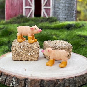 May include: Two miniature pig figurines wearing yellow rain boots. The pigs are standing on hay bales.