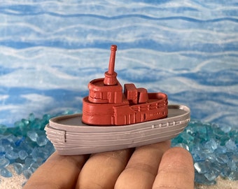 Könnte beinhalten: Ein kleines, rotes und graues Spielzeugschleppboot mit einem erhöhten Deck und einem einzelnen Schornstein. Das Boot liegt auf einer Hand.
