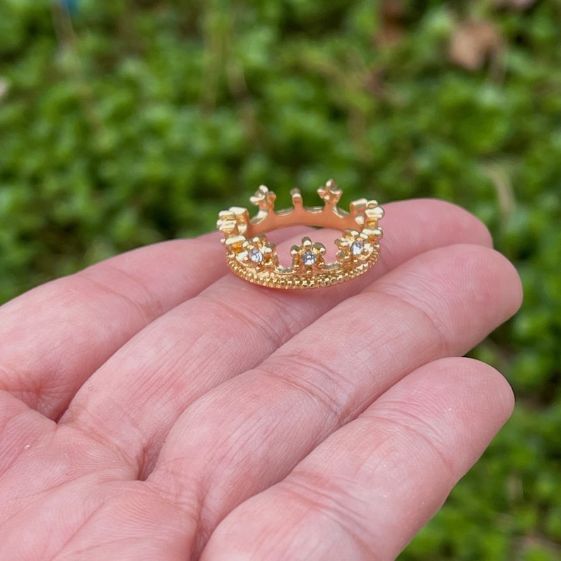 May include: A gold crown ring with clear cubic zirconia stones.