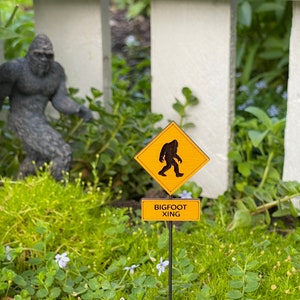 May include: A yellow warning sign with a black silhouette of Bigfoot walking, with the text "BIGFOOT XING" on a smaller sign below.