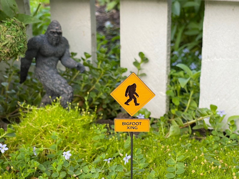 May include: A yellow warning sign with a black silhouette of Bigfoot walking, with the text "BIGFOOT XING" on a smaller sign below.