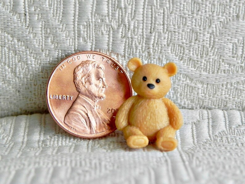 May include: A miniature tan teddy bear with black eyes and a black nose sits next to a U.S. penny. The bear is approximately 1 inch tall. The penny shows the profile of Abraham Lincoln and the words "In God We Trust."