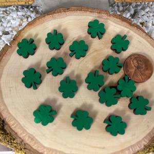 May include: A close-up of a wooden board with 17 green shamrock shapes scattered across the surface. A penny is placed on the board for scale.