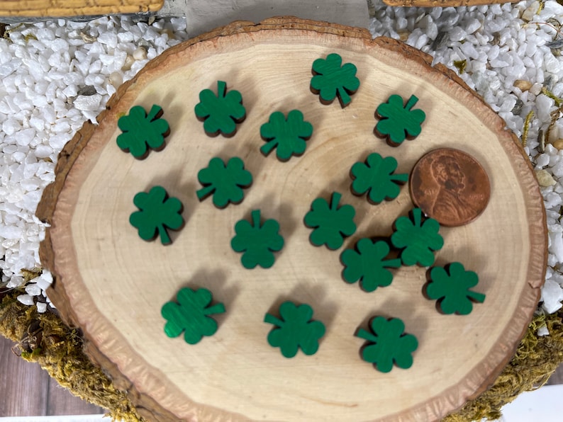 May include: A close-up of a wooden board with 17 green shamrock shapes scattered across the surface. A penny is placed on the board for scale.