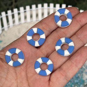 May include: Five miniature blue and white life preservers. Each ring is a small circle with alternating blue and white segments. The objects are held in a person's hand, with a blurred background.