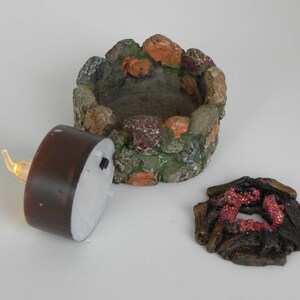 May include: A miniature stone fire pit with a brown tea light candle and a separate piece of faux wood with red glitter accents.