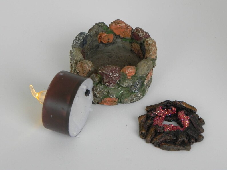 May include: A miniature stone fire pit with a brown tea light candle and a separate piece of faux wood with red glitter accents.