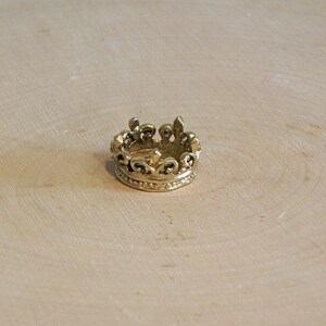 May include: A gold-colored crown ring with a detailed design. The ring is made of metal and has a smooth finish.