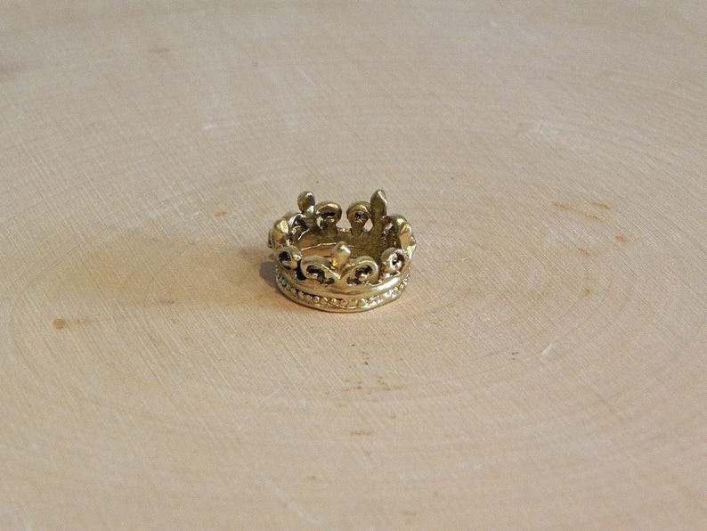 May include: A gold-colored crown ring with a detailed design. The ring is made of metal and has a smooth finish.