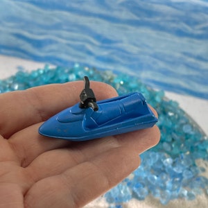 May include: A small blue toy jet ski with a black handle. The jet ski is sitting on a hand.