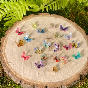 May include: A collection of colorful butterfly-shaped embellishments on a wooden surface. The butterflies are made of various materials, including paper, fabric, and plastic. They are arranged in a random pattern, creating a whimsical and decorative display.