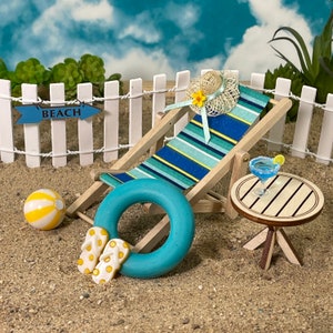 May include: A miniature beach scene with a blue and white striped beach chair, a blue inflatable ring, yellow and white beach ball, a small wooden table with a blue margarita glass, and a sign that says "BEACH".