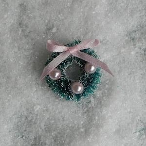 May include: A small green Christmas wreath with a pink bow and white pearl ornaments.