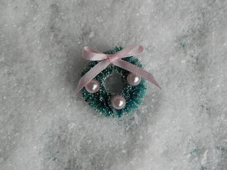 May include: A small green Christmas wreath with a pink bow and white pearl ornaments.