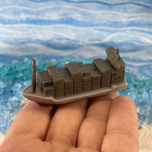 May include: A miniature gray cargo ship with a brown cargo container deck. The ship is sitting on a hand.